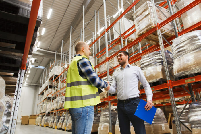 wholesale, logistic, people and export concept - manual worker and businessmen with clipboard shaking hands and making deal at warehouse